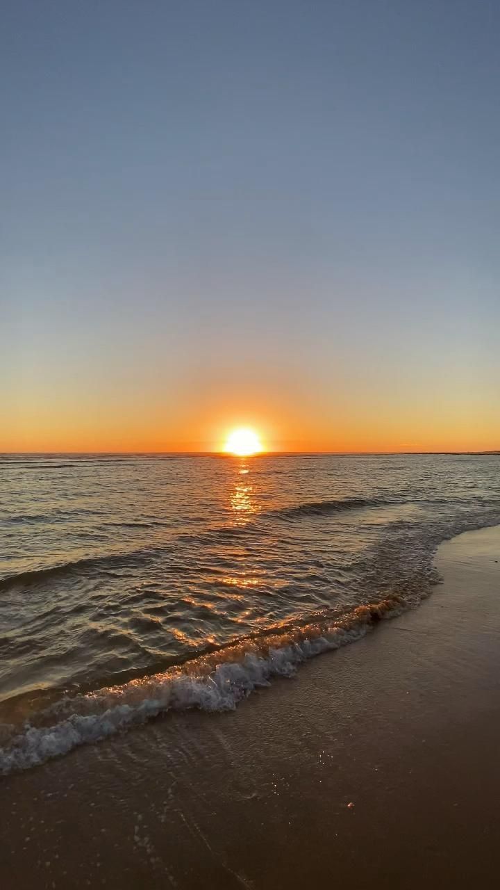 the sun is setting over the water at the beach with waves coming in to shore