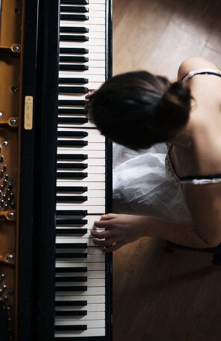 a woman kneeling down next to an open piano with her hands on the keys and looking at it