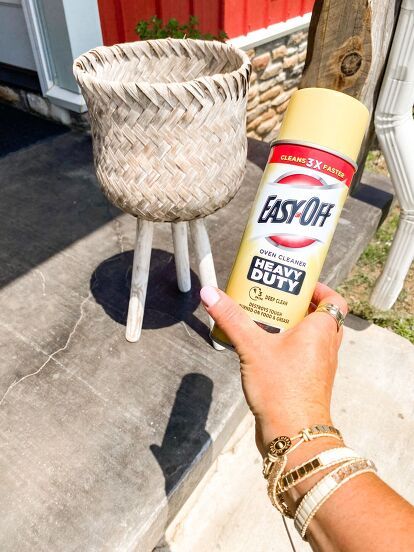 a person holding a spray bottle in front of a potted plant on the sidewalk