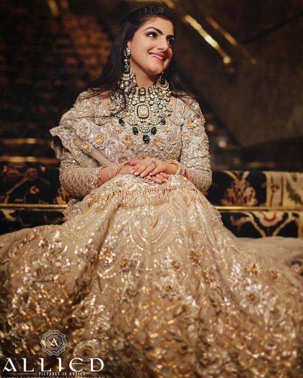 a woman sitting on top of a bed wearing a gold dress and necklace with jewels