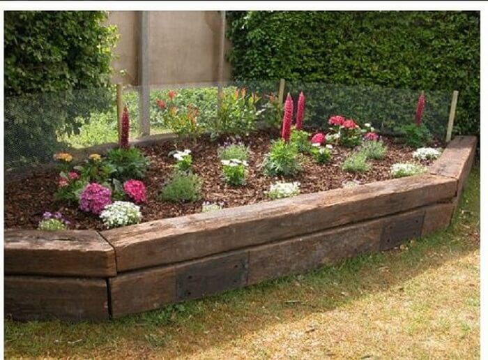 a wooden garden bed with flowers and plants growing in the top row, along side a building