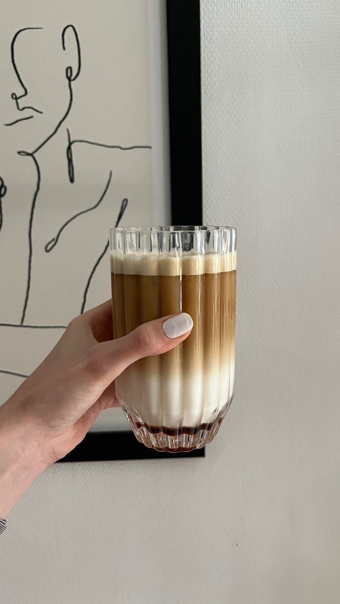 a hand holding a glass filled with liquid in front of a drawing on the wall