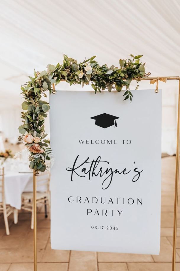 a welcome sign for a graduation party with greenery on it and a white backdrop