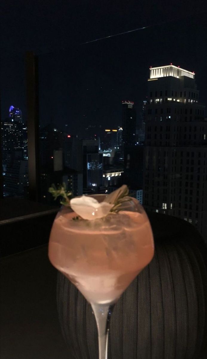 a tall glass filled with a drink on top of a table in front of a cityscape