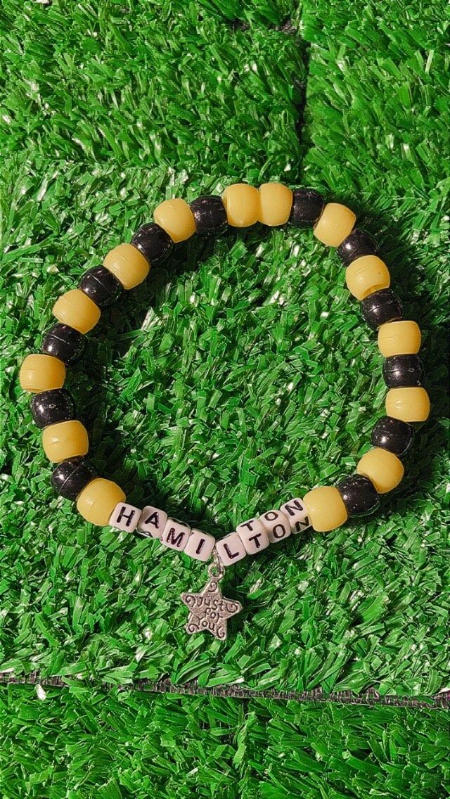 a yellow and black beaded bracelet with a cross on it, sitting in the grass