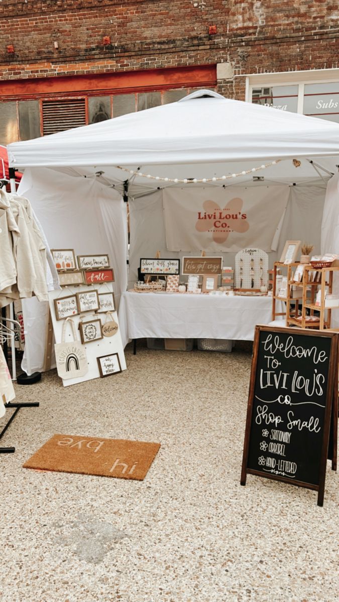 an outdoor market with white tents and pictures on the table, signs for sale and other items