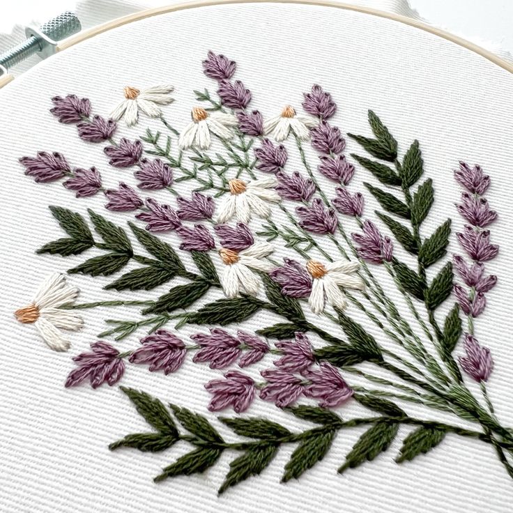 some white and purple flowers with green leaves on the bottom right hand side is an embroidery pattern