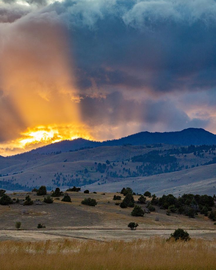 the sun is shining through the clouds in the sky over some hills and trees with mountains in the background