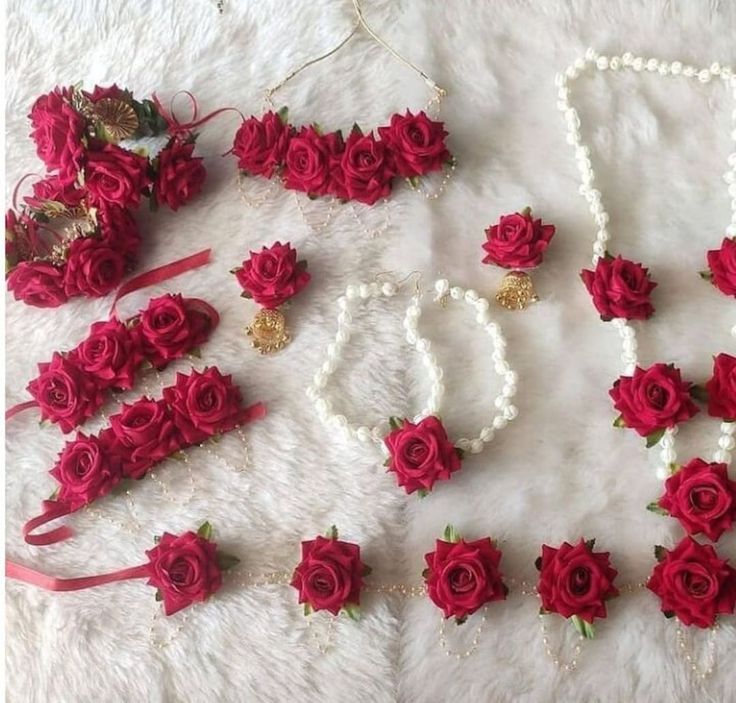 red roses and pearls are laid out on a white furnishing with beaded necklaces