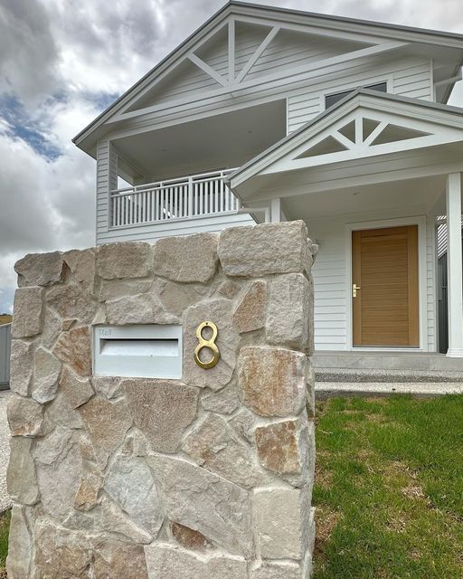 a white house with a brown door and numbers on the stone wall in front of it