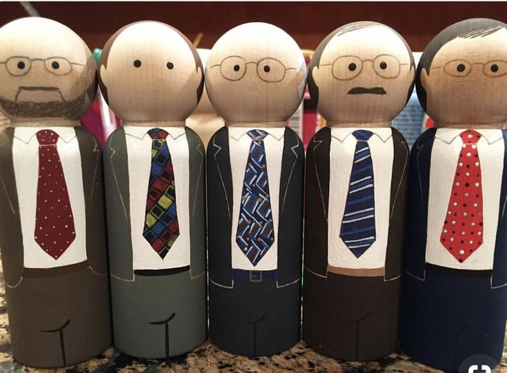 five paper dolls in suits and ties are lined up on a countertop, with one man's face drawn to the side