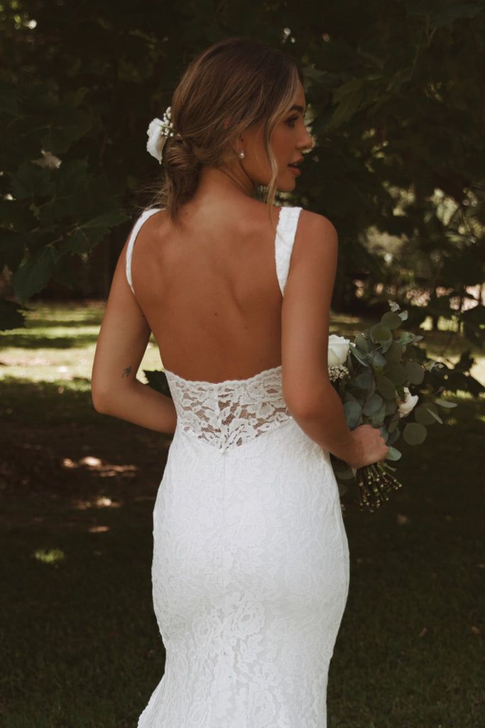 a woman in a white wedding dress holding a bouquet and looking back at the camera