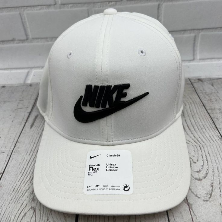 a white hat with black nike logo on it sitting on a wooden floor next to a brick wall