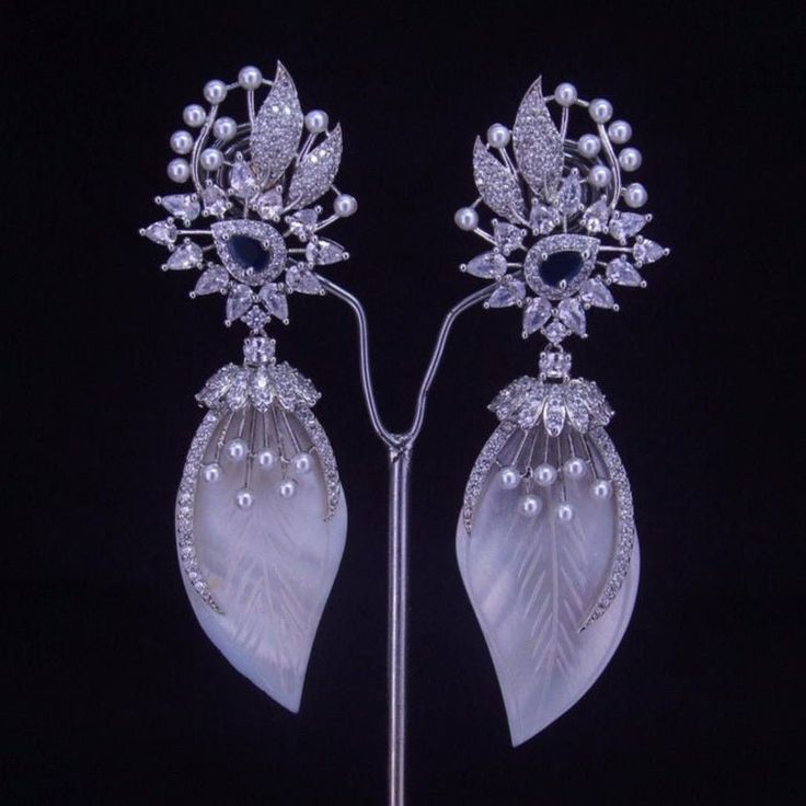 Add a touch of sophistication to your ensemble with our Blue Centerpiece earrings. Adorned with a lustrous silver pearl, these white stone earrings are the perfect accessory for any occasion. Elevate your style and make a statement today. Our CZ Jewelry Sets are the most difficult ones to make. It takes over 80 hours of Design work to design each of these handcrafted Masterpieces. Handcrafted in India by the finest Diamond Jewelry Craftsmen from West Bengal. Diamond-Like Brilliance: Enhanced with diamond CZ accents, the stones sparkle with brilliance and add a touch of glamour to the set. Versatile Elegance: Suitable for bridal wear, formal events, or any occasion where a touch of class is desired, this set promises to elevate any look with its timeless beauty. Impeccable Craftsmanship: Me Formal White Cubic Zirconia Chandelier Earrings, White Cubic Zirconia Chandelier Earrings For Formal Events, White Cubic Zirconia Chandelier Earrings For Formal Occasions, White Diamond Chandelier Earrings For Party, Exquisite White Diamond Earrings For Evening, White Glamorous Diamond Dangle Earrings, White Diamond Crystal Drop Earrings, Glamorous White Diamond Dangle Earrings, Glamorous White Diamond Earrings