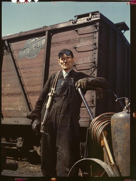 an old man standing in front of a train with his hand on the handlebars