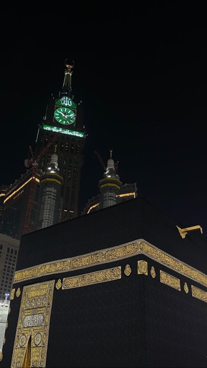 the clock tower is lit up at night in front of other buildings and skyscrapers