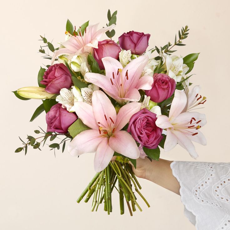 a woman holding a bouquet of pink and white flowers in her left hand, on a beige background