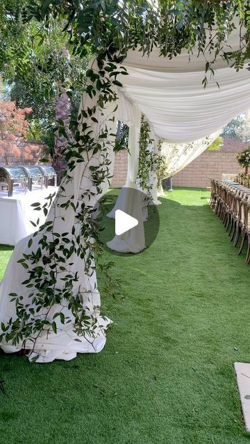 an outdoor ceremony setup with white drapes and greenery