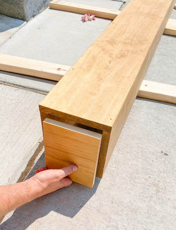 a hand reaching for a piece of wood that is attached to the side of a bench