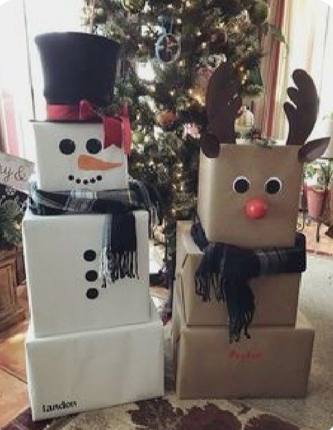 two cardboard boxes decorated like snowmen sitting in front of a christmas tree