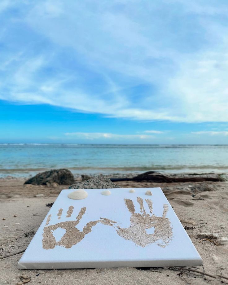 a white board with two hand prints on it sitting in the sand at the beach