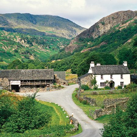 an old country house in the middle of a green valley with mountains in the background