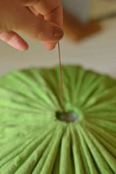 a person is holding a green fan with pins in it's center and pointing to the top