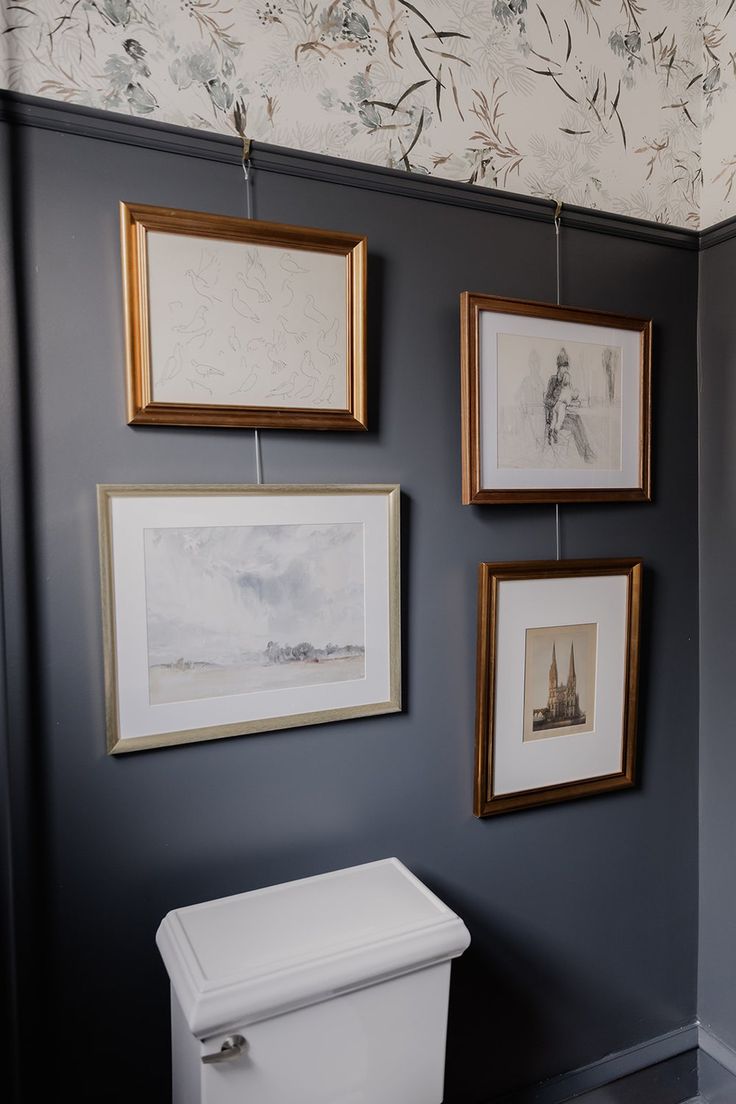 three framed pictures hang on the wall above a toilet in a bathroom with gray walls