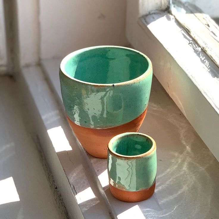 two green and brown bowls sitting on top of a window sill next to each other