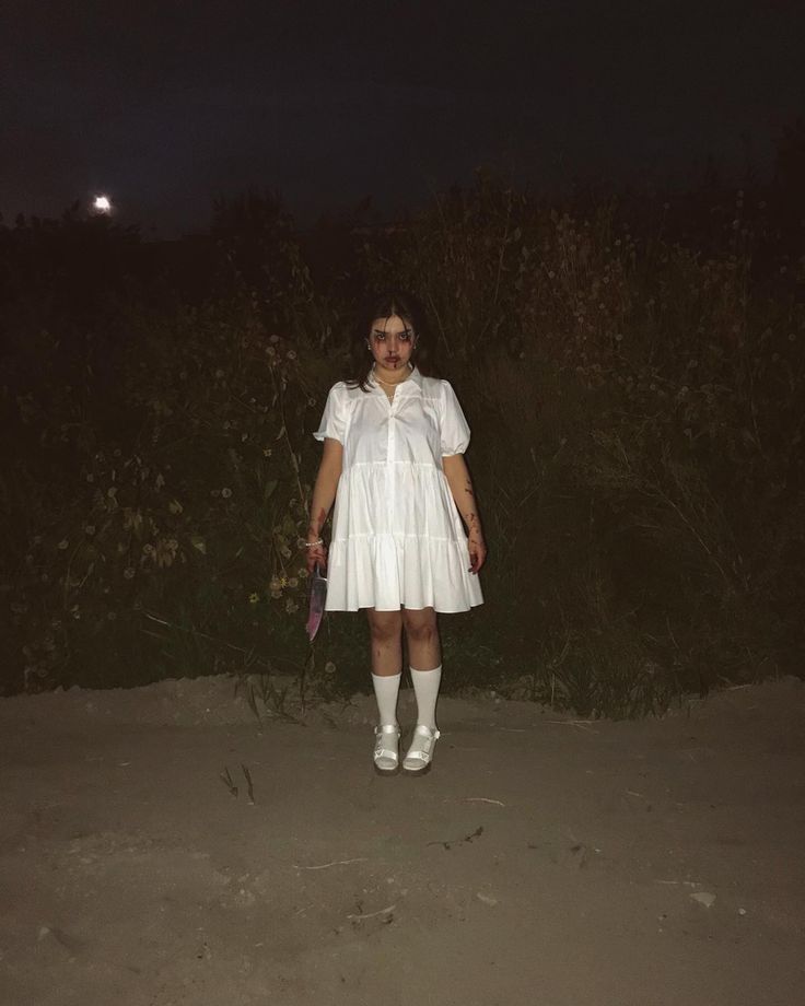 a woman in a white dress and socks standing on the sand at night with a knife