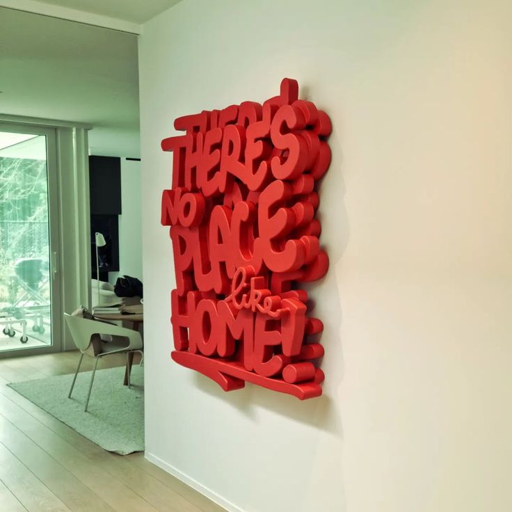 there is a red sculpture on the wall in this living room that says, here's no place to be home