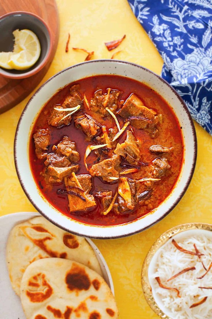 a bowl filled with meat and sauce next to tortilla bread on a yellow table cloth