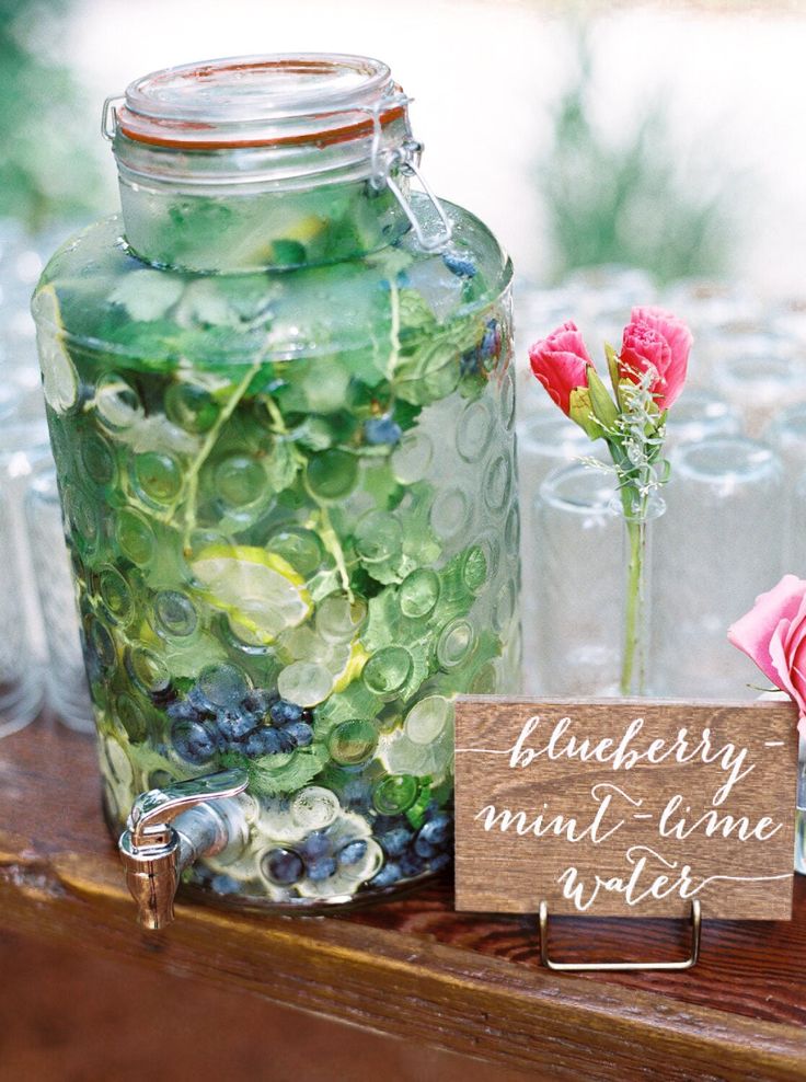 a table topped with lots of glass bottles filled with water and flowers next to a wooden sign