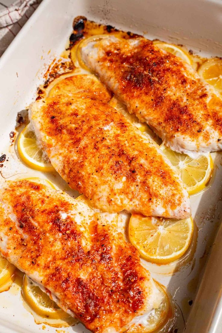 two pieces of chicken with lemons and seasoning in a baking dish