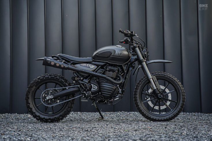 a black motorcycle parked in front of a metal wall with gravel on the ground next to it