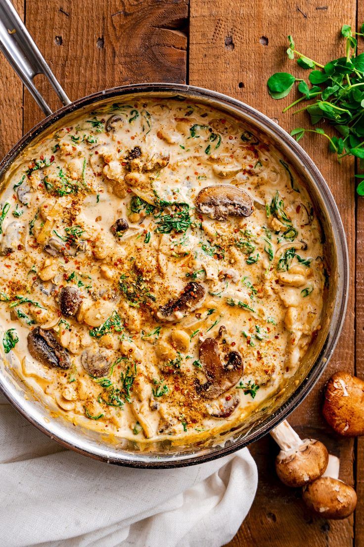 a pan filled with pasta and mushrooms on top of a wooden table next to garlic