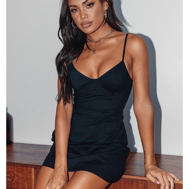 a woman sitting on top of a wooden table wearing a black dress and high heels