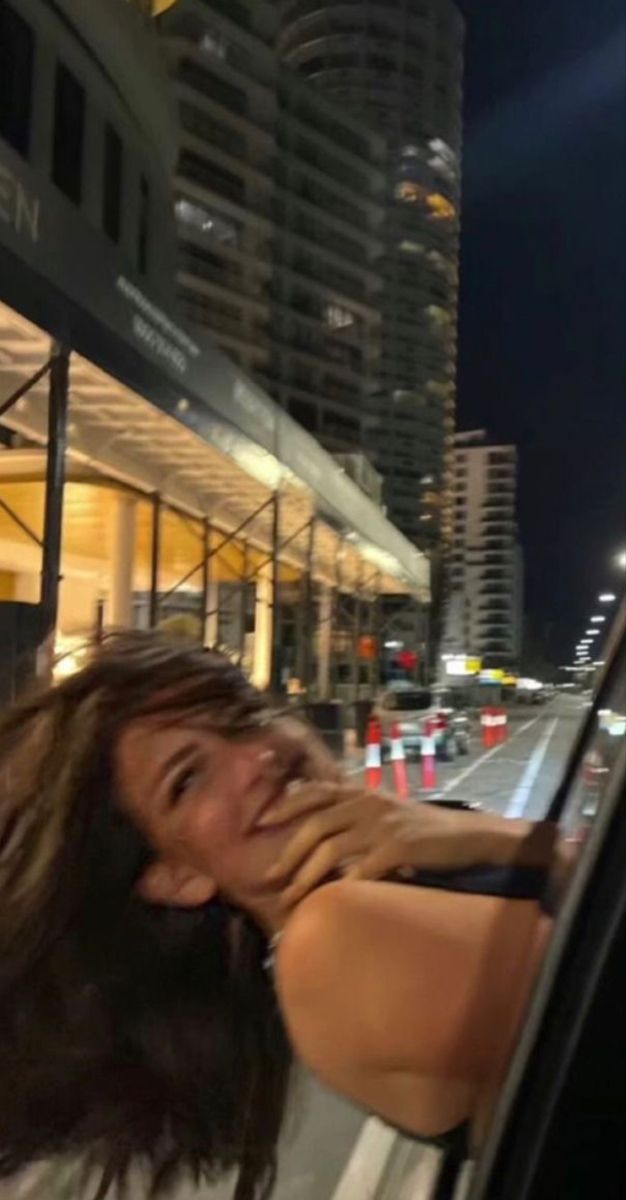 a woman leaning out the window of a car in front of a building at night