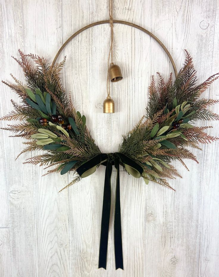 a wreath hanging on the wall with bells and greenery in front of white wood planks