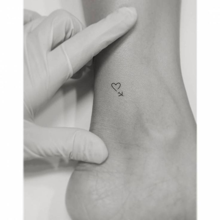 someone is holding their foot up to show the tiny heart tattoo