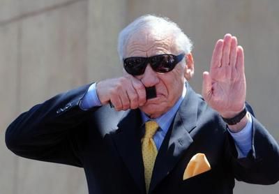 an older man in a suit and sunglasses making a hand gesture with his right hand