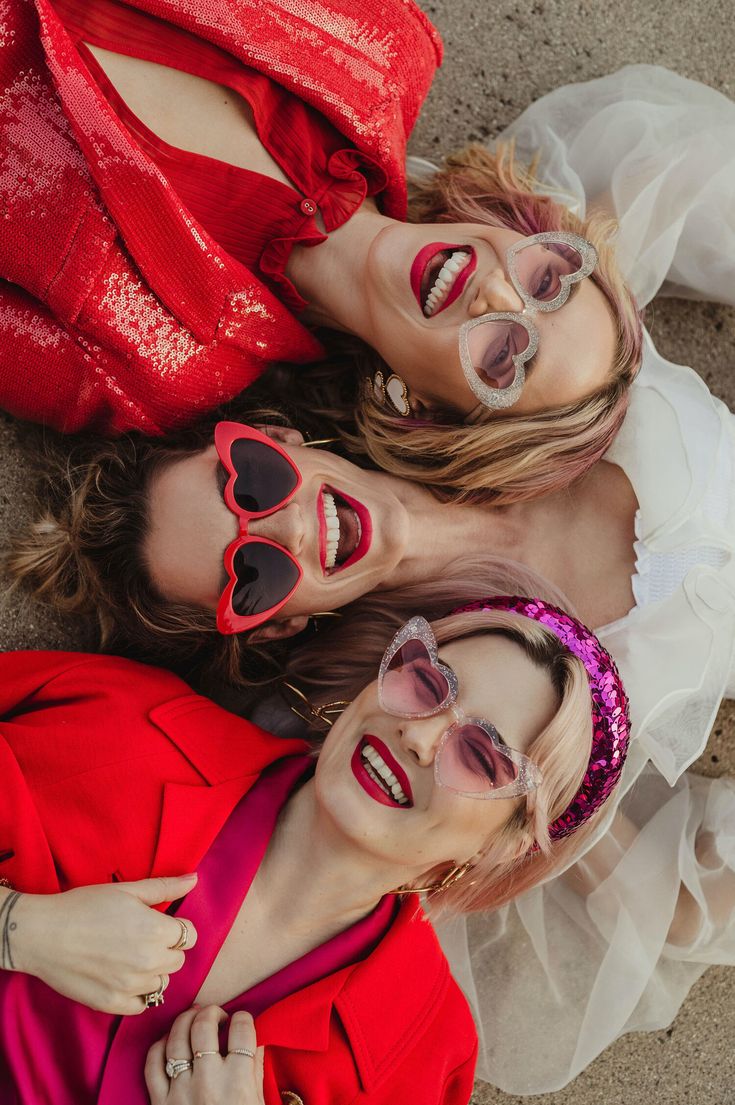 three women wearing heart shaped sunglasses laying on the ground