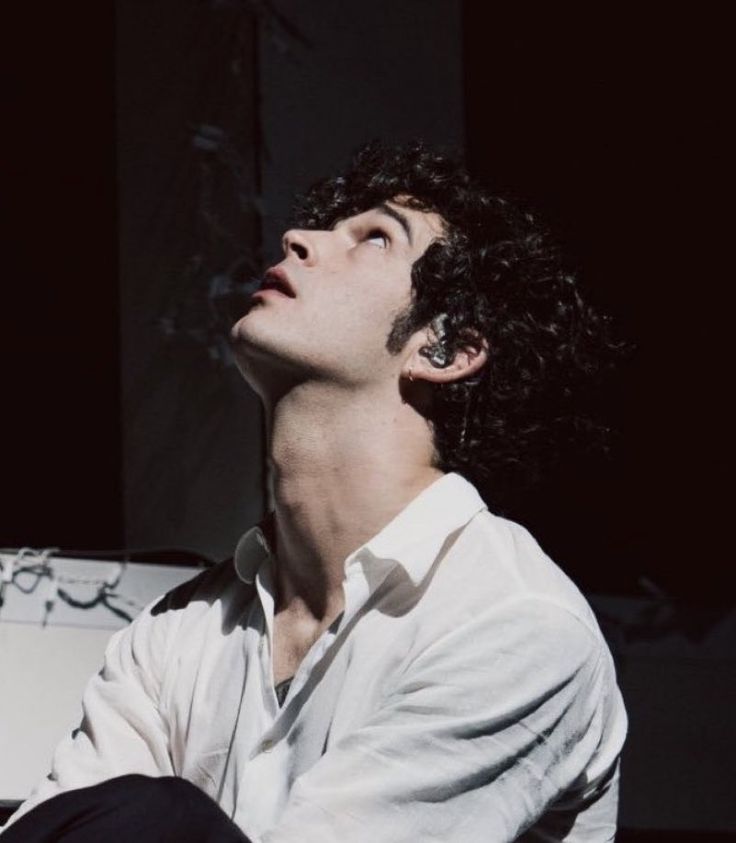 a man with curly hair sitting down and looking up at something in the air above his head