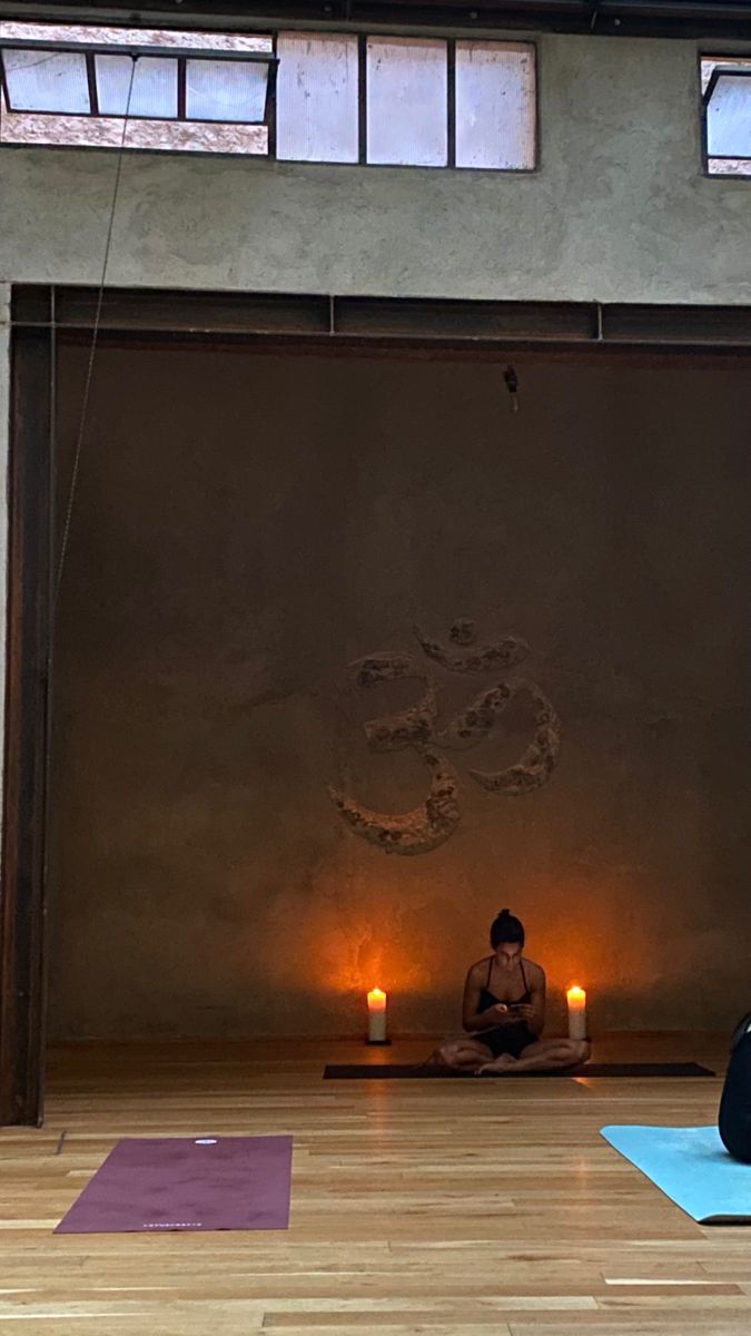 a woman sitting in the middle of a yoga class with candles lit up behind her