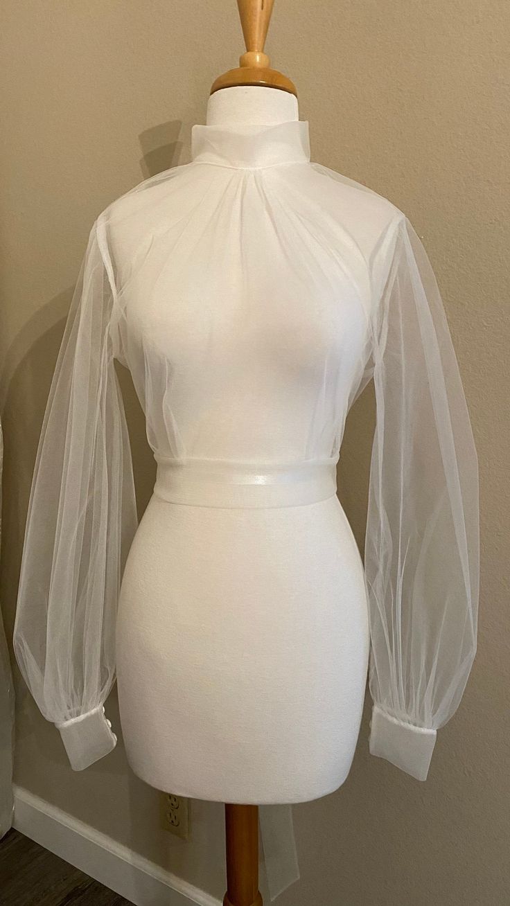 "Tulle wedding dress topper Mock turtle neckline with covered button closure at back neck Open 'V' back with long ties at back waist Bishop sleeves with cuffs/covered buttons **Made to order** Available up to 40\" bust Choose off-white or pale ivory - or ask for a specific color! Rush orders available - please ask about pricing & timing!" High Neck Fitted Party Blouse, Elegant Fitted Tops For Weddings, Fitted High Neck Blouse For Party, High Neck Fitted Blouse For Party, Elegant High Neck Fitted Blouse, Elegant High Neck Tops With Mesh Sleeves, White Fitted Blouse With Sheer Sleeves, Elegant Stretch Tops For Wedding, Wedding Dress With Sheer Bishop Sleeves