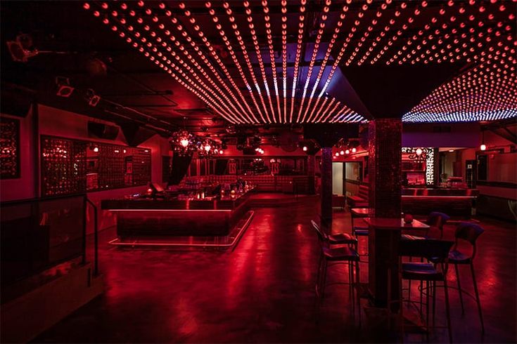 a dimly lit room with red and blue lights on the ceiling, couches and bar stools