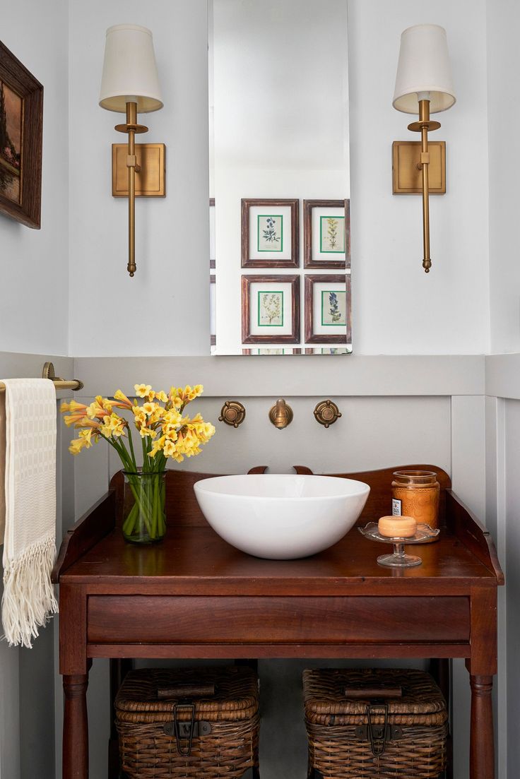 a bathroom sink sitting under a mirror next to a wooden table with baskets on it