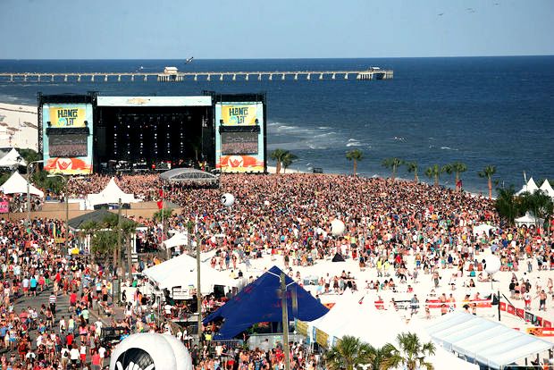 a large group of people at an outdoor concert on the beach, with one stage in the background