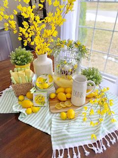 a table topped with lemons and flowers next to a vase filled with yellow flowers