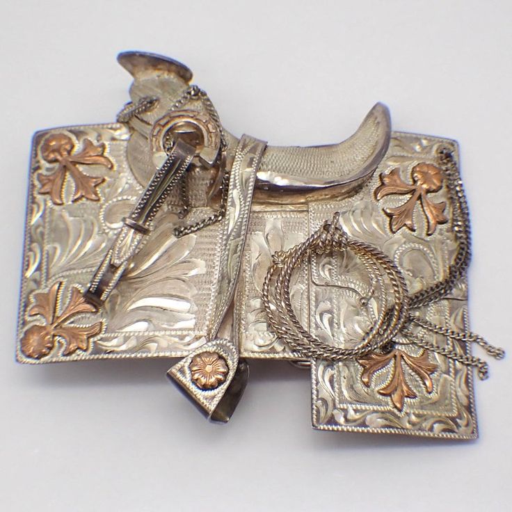 Vintage figural sterling silver belt buckle, featuring horse saddle with attached gadgets. It is decorated with bright cut engraved patterns and applied 10k (.417) yellow gold elements. This outstanding buckle is 4 1/8" long, 3 7/8" wide, weighing 159.4 grams or 5.14 ozs Troy. EA4941 Gold Western Belt Buckles For Formal Wear, Gold Western Belt Buckles For Formal Occasion, Formal Gold Engraved Belt Buckles, Gold Concho Belt Buckle For Formal Occasions, Antique Engraved Belt Buckles For Formal Wear, Western Style Jewelry With Silver Buckle For Formal Occasions, Formal Western Jewelry With Silver Buckle, Vintage Silver Hand Tooled Belt Buckles, Antique Engraved Belt Buckles For Gift